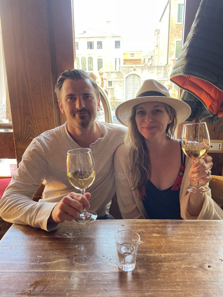 A couple holds glasses full of white wine sitting at a table at Al Timon in the Cannaregio in Venice